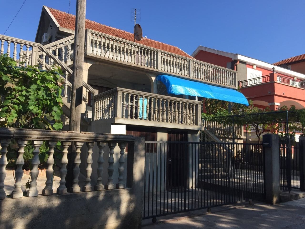 Двухэтажный дом с террасами и балюстрадами в поселке Крымовица, Черногория: вид на фасад с ограждением и виноградником.