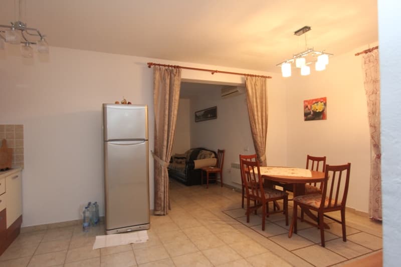 Интерьер кухни-гостиной в квартире в Бечичи, Черногория: обеденная зона, холодильник и проход в комнату с диваном.