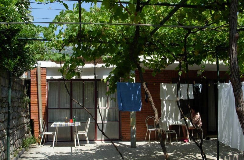 Уютная терраса дома в Бечичи, Черногория, с виноградной лозой, садовой мебелью и зоной отдыха у кирпичного фасада.