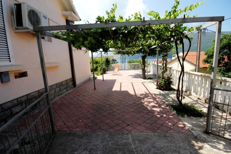 Терраса с виноградной перголой у дома в Дженовичи, Черногория: вид на море, мощеная площадка и зона отдыха.