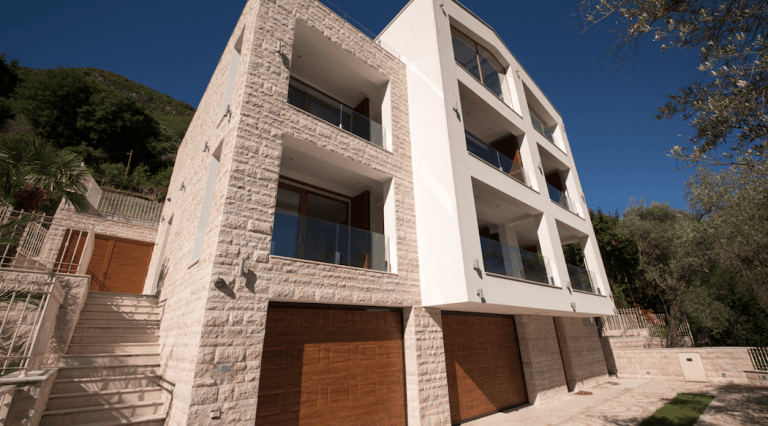 Современный дом в Столиве, Черногория: фасад из камня, панорамные балконы с остеклением и гаражные ворота из дерева.