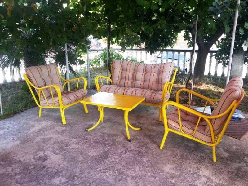 Уютная зона отдыха с желтой садовой мебелью в тени виноградника у дома в Сутоморе, Черногория.