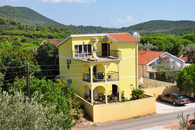 Трехэтажный желтый дом с террасами и видом на горы в Луштице, Черногория: частная парковка и зеленый сад.