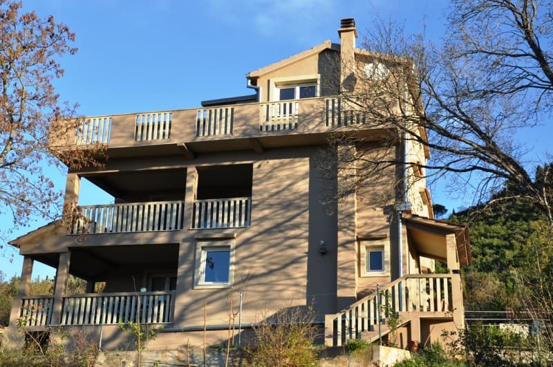 Трехэтажный дом с террасами и балконами на полуострове Луштица, Черногория. Фасад здания в окружении деревьев.