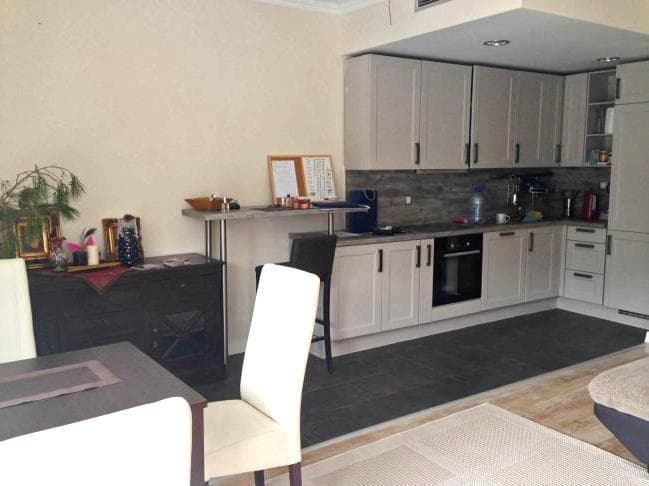 Современная кухня-гостиная в квартире в Доброте, Черногория: светлый гарнитур, барная стойка и обеденная зона.