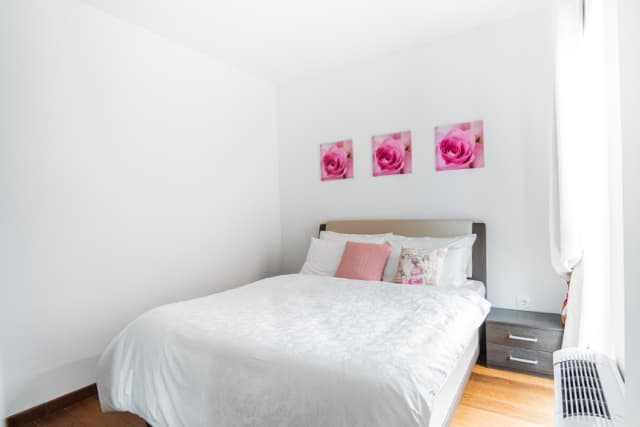 Светлая спальня с двуспальной кроватью в квартире в Будве, Черногория: паркет, картины с розами, прикроватная тумба.