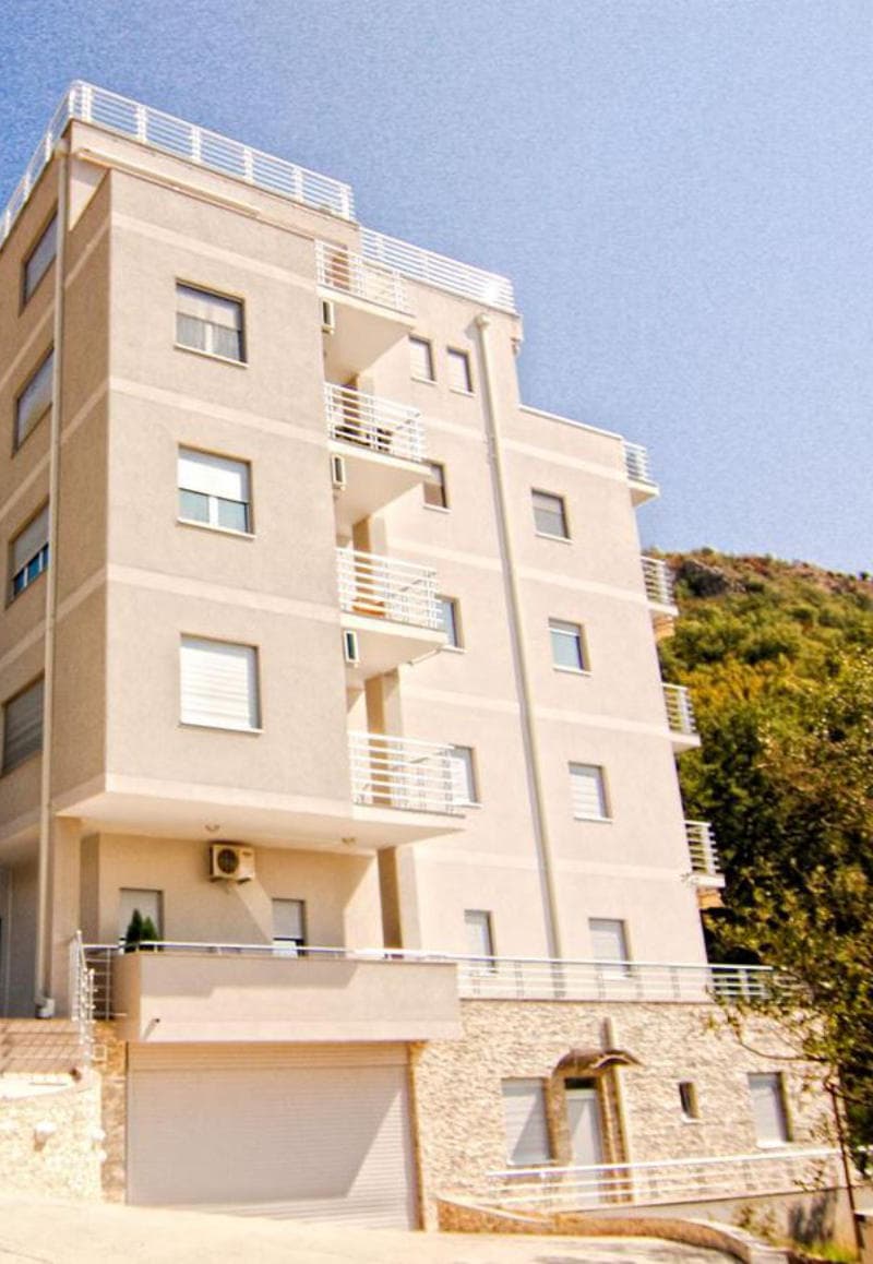 Современный многоквартирный дом с балконами в Бечичи, Черногория: фасад здания с отделкой камнем и светлой штукатуркой.