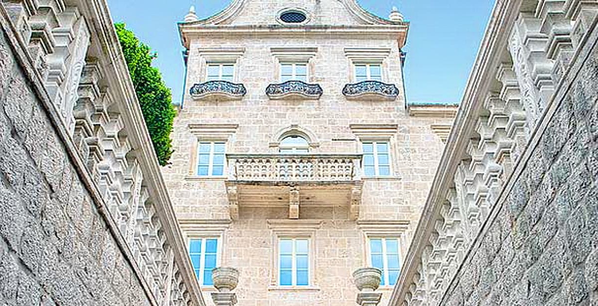 Фасад исторической каменной виллы в Доброте, Черногория: классическая архитектура, балкон и резные элементы декора.