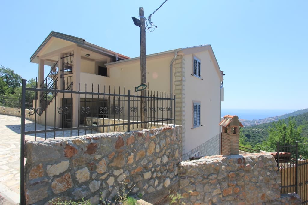Двухэтажный дом в Будве, Черногория, с каменным забором, террасой и панорамным видом на море и горы.
