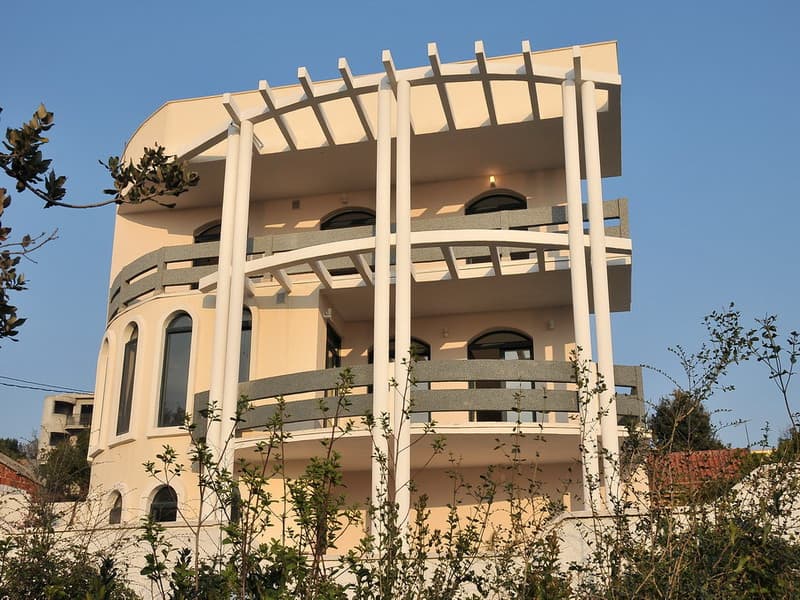 Трехэтажный дом в Утехе, Черногория: современный фасад с колоннами, арочными окнами и просторными террасами.