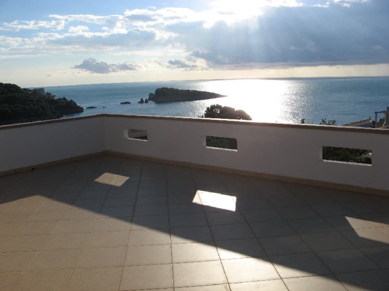 Просторная терраса с видом на море и остров в Утехе, Черногория: плиточное покрытие и белые ограждения дома.