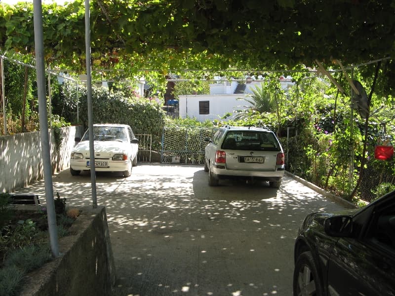 Частная парковка во дворе дома в Шушани, Черногория, с навесом из виноградной лозы и местами для автомобилей.