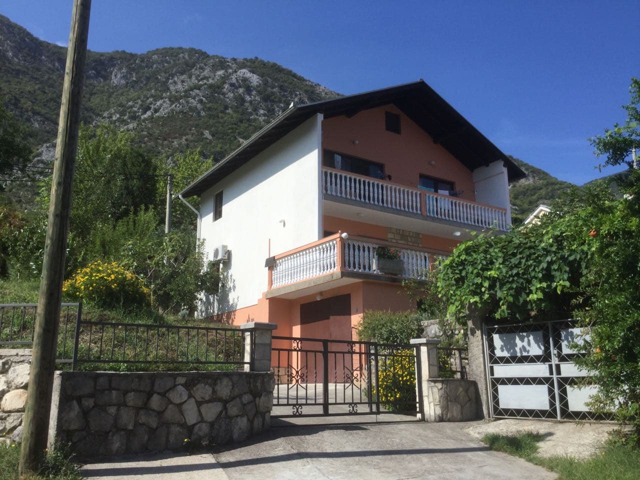 Двухэтажный дом с балконами и гаражом в Прчани, Черногория, на фоне горного пейзажа и зеленого сада.