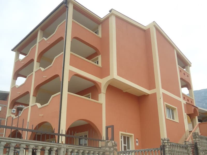 Трехэтажный дом в Шушани, Черногория: фасад персикового цвета с открытыми террасами и арочными элементами.