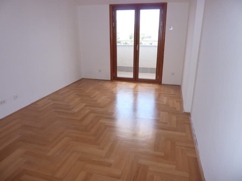 Светлая пустая комната с паркетом «елочка» и выходом на балкон в квартире, Тиват, Черногория.