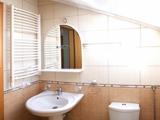 Ванная комната в квартире в Зеленике, Черногория: бежевая плитка, раковина, зеркало и полотенцесушитель в мансарде.