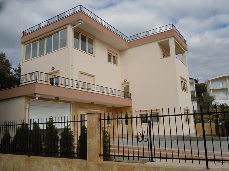 Трехэтажный дом в Будве, Черногория: современный фасад с террасами, панорамными окнами и кованым ограждением.