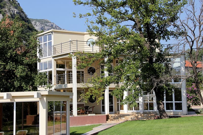 Трехэтажный дом с панорамными окнами и террасами в Сутоморе, Черногория, окруженный зеленью и горами.