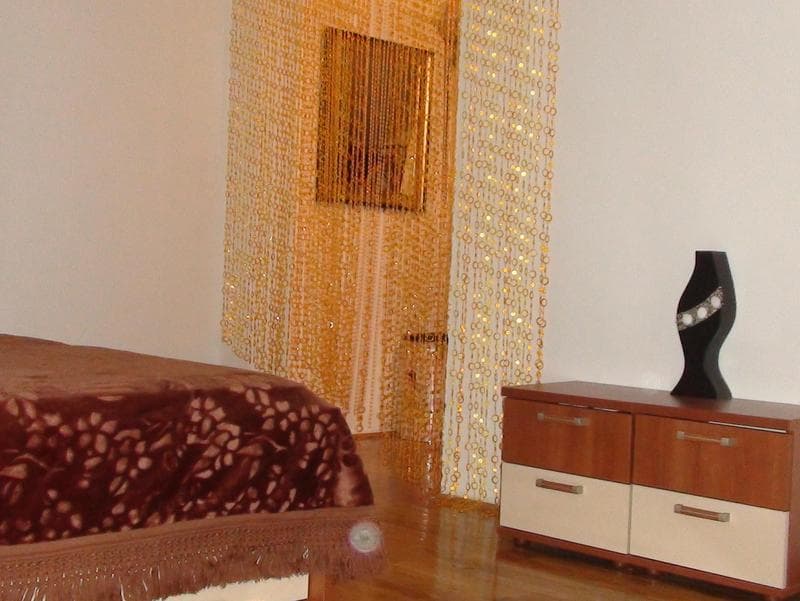 Интерьер спальни в квартире в Будве, Черногория: двуспальная кровать, комод и декоративная штора из золотистых бусин.