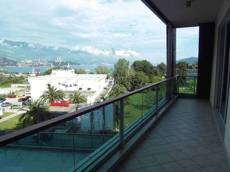 Вид с террасы квартиры в Будве, Черногория: панорама на море, горы и город с просторного балкона с ограждением.