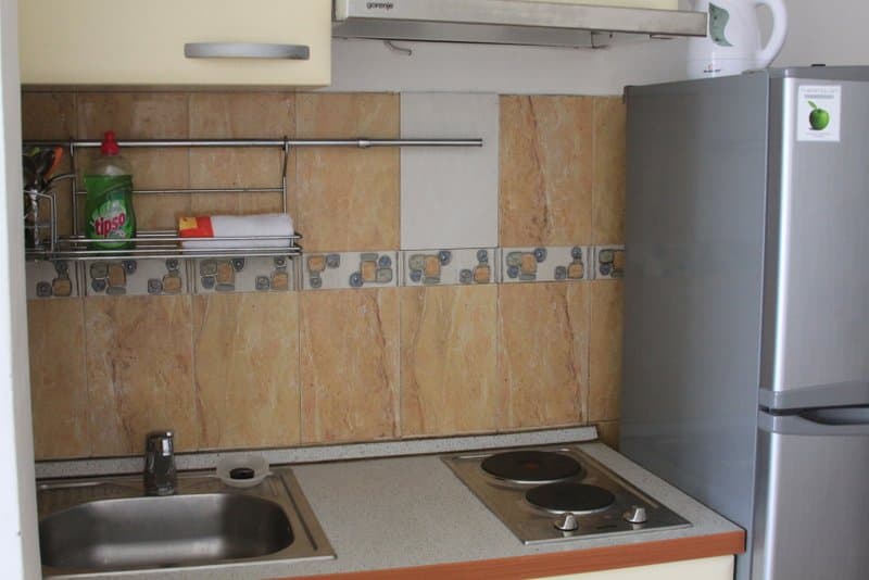 Компактная кухня в апартаментах Рафаиловичи, Черногория: мойка, электроплита, холодильник и плиточный фартук.