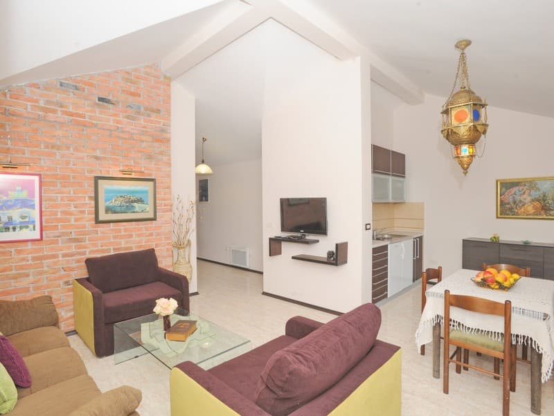 Интерьер гостиной с кирпичной стеной и кухней на вилле в Бигово, Черногория: мягкая мебель, обеденная зона и декор.