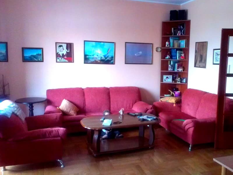 Уютная гостиная с красными диванами и стеллажом в квартире в Будве, Черногория. Интерьер с картинами и паркетом.