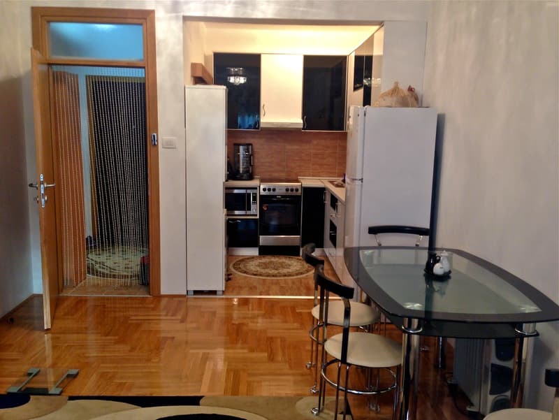 Современная кухня с обеденной зоной в квартире, Будва, Черногория: стеклянный стол, темные фасады и паркетный пол.