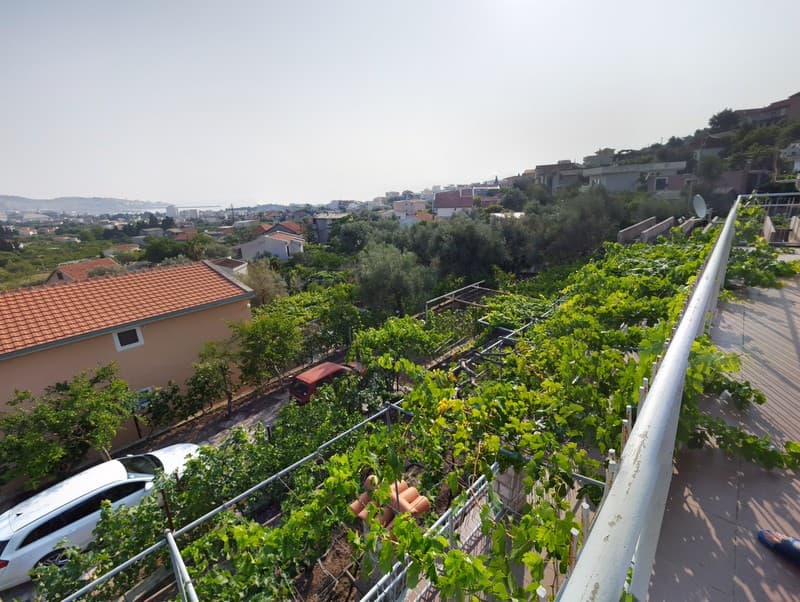 Вид с террасы дома в Шушани, Черногория: зеленый виноградник, придомовая территория и панорама города.