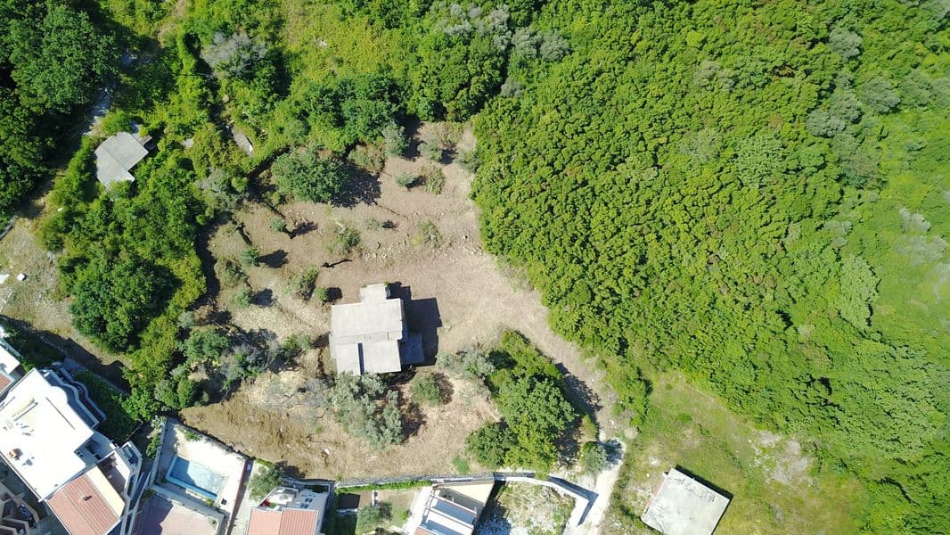 Вид с дрона на земельный участок под застройку в Бечичи, Черногория, окруженный густым лесом и оливковыми деревьями.
