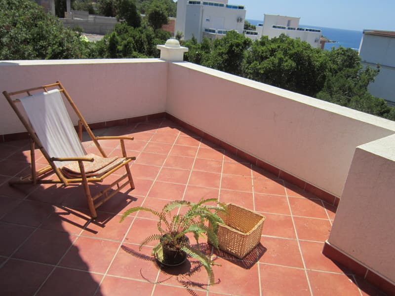 Терраса с видом на море в доме, Утеха, Черногория: бамбуковый шезлонг, плиточный пол и комнатное растение.