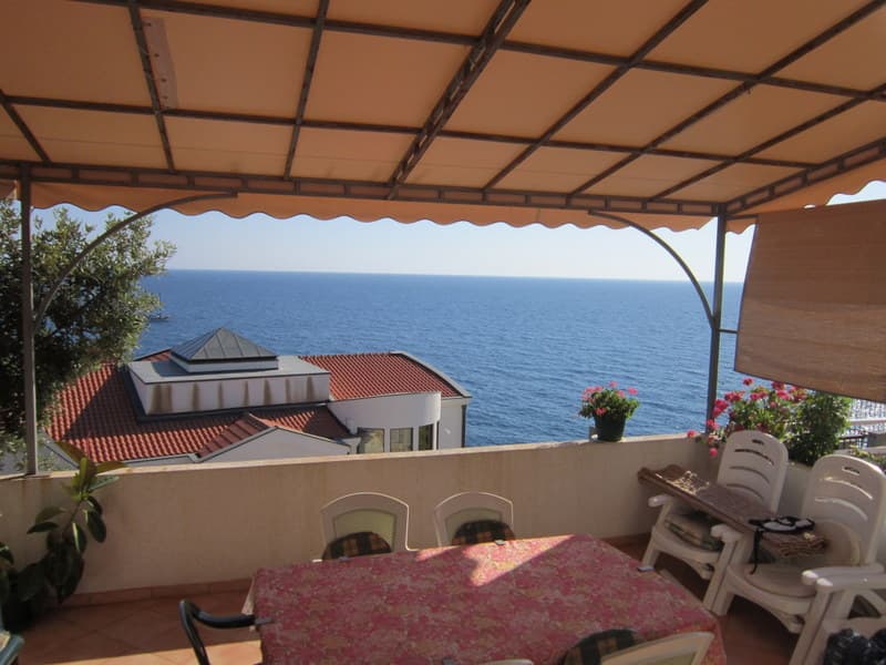 Терраса с видом на море в доме в Утехе, Черногория: пластиковая мебель, навес и панорамный морской пейзаж.