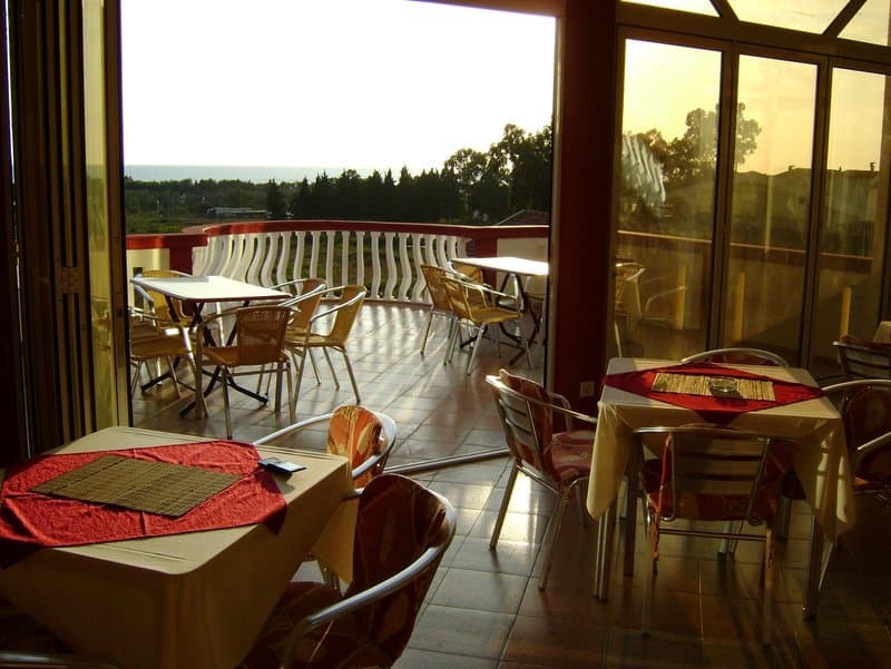 Терраса отеля в Баре, Черногория: столики с видом на море, плетеная мебель и панорамное остекление ресторана.