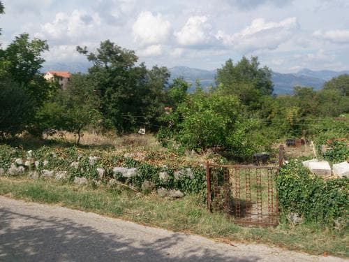 Земельный участок в Луштице, Черногория: вид на территорию с каменной оградой, деревьями и горным пейзажем.