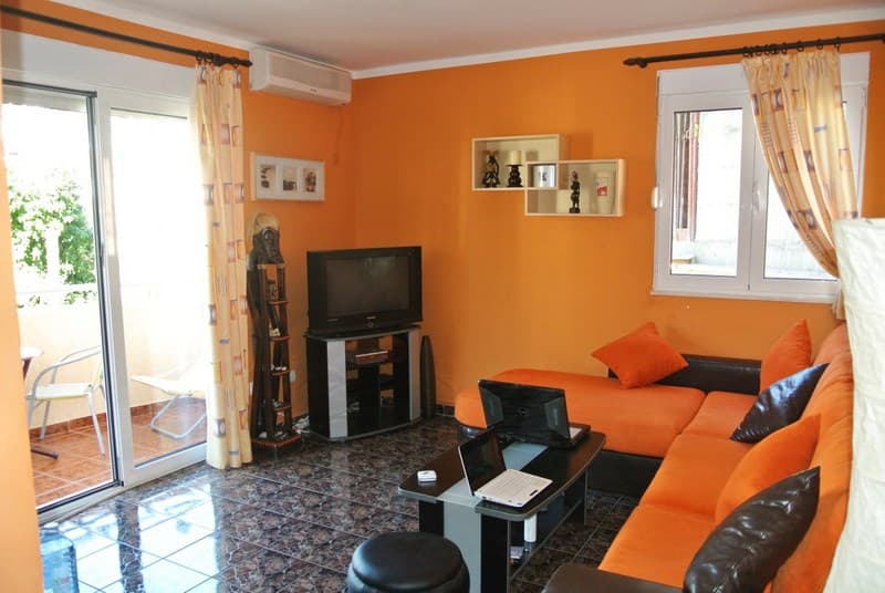 Гостиная с оранжевыми стенами, угловым диваном и выходом на балкон в квартире в Будве, Черногория.