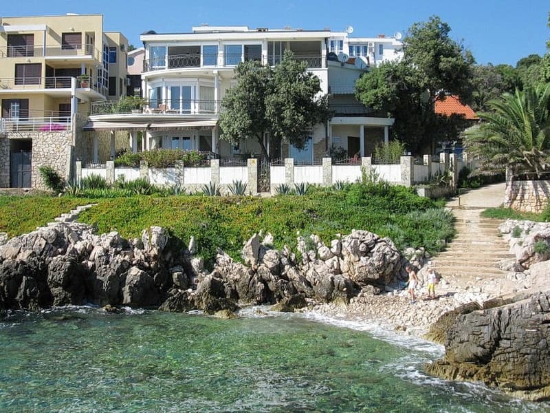 Вилла на первой линии моря в Добрых водах, Черногория: вид на дом с террасами, скалистый берег и частный спуск к пляжу.