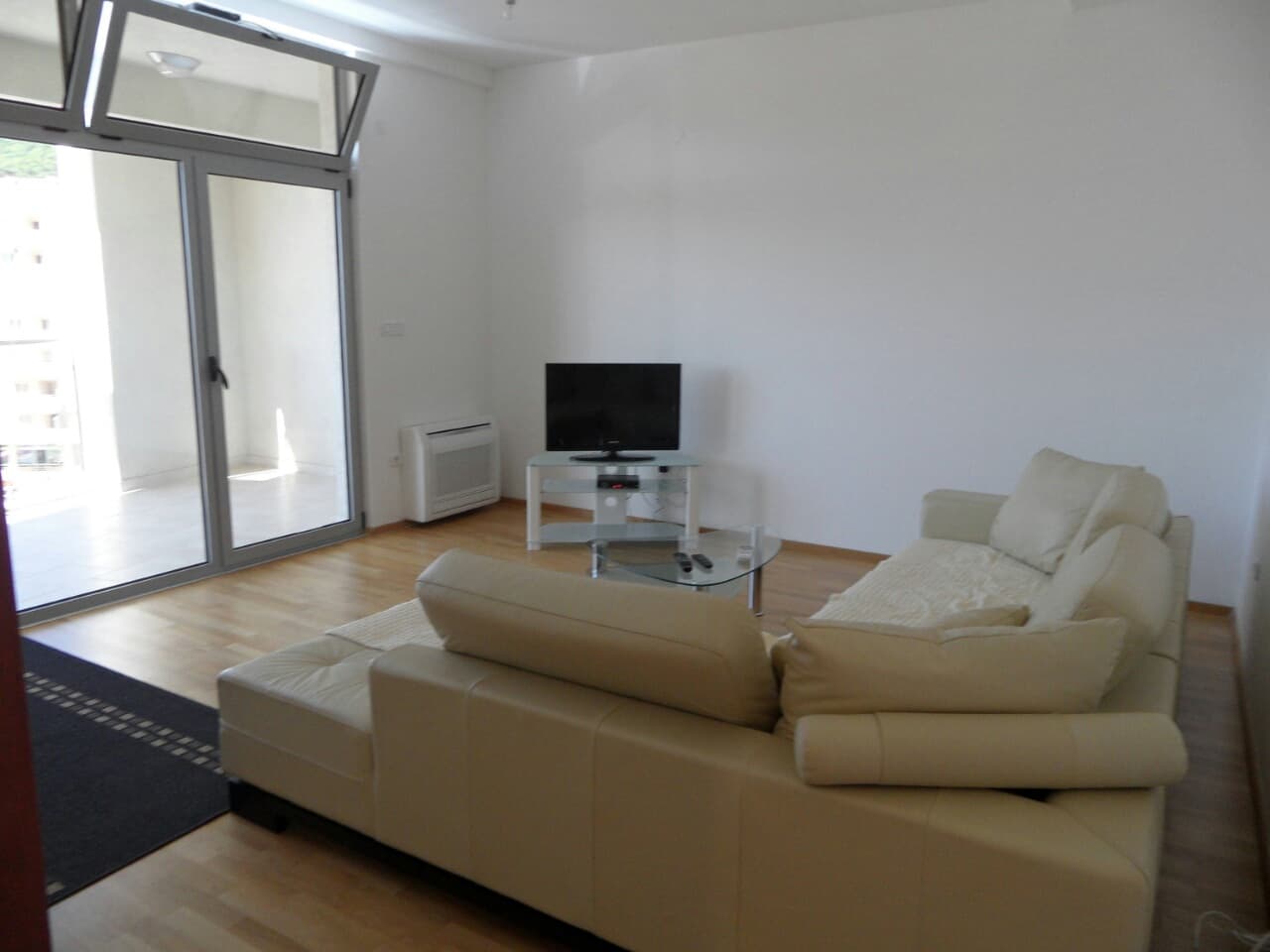 Светлая гостиная с кожаным диваном и выходом на террасу в квартире в Будве, Черногория. Современный интерьер с ТВ.