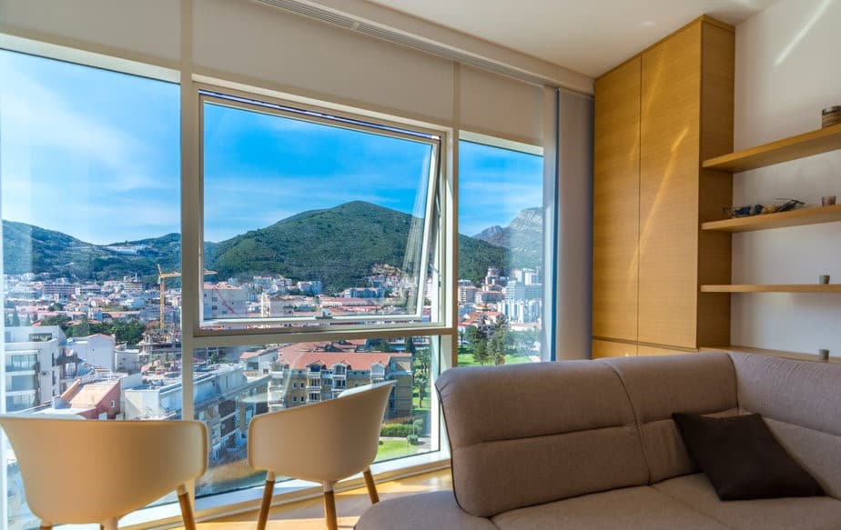 Современная гостиная в квартире в Будве, Черногория, с панорамным видом на горы и город через большие окна.