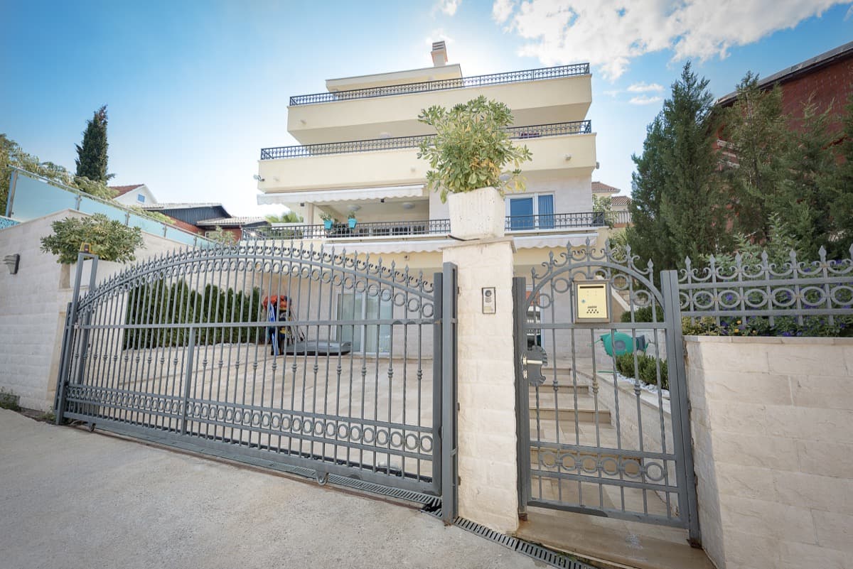 Трехэтажная вилла в Крашичи, Черногория: фасад с коваными воротами, каменной отделкой и террасами с ограждениями.