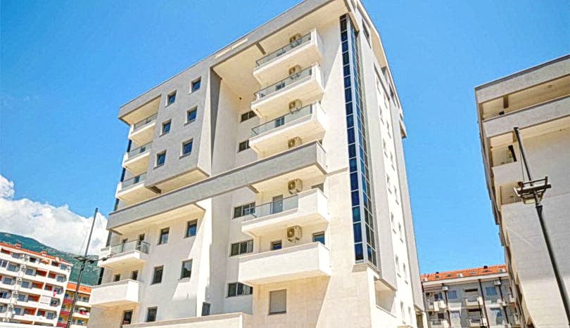 Современный многоэтажный жилой комплекс в Будве, Черногория: светлый фасад, панорамное остекление и балконы.