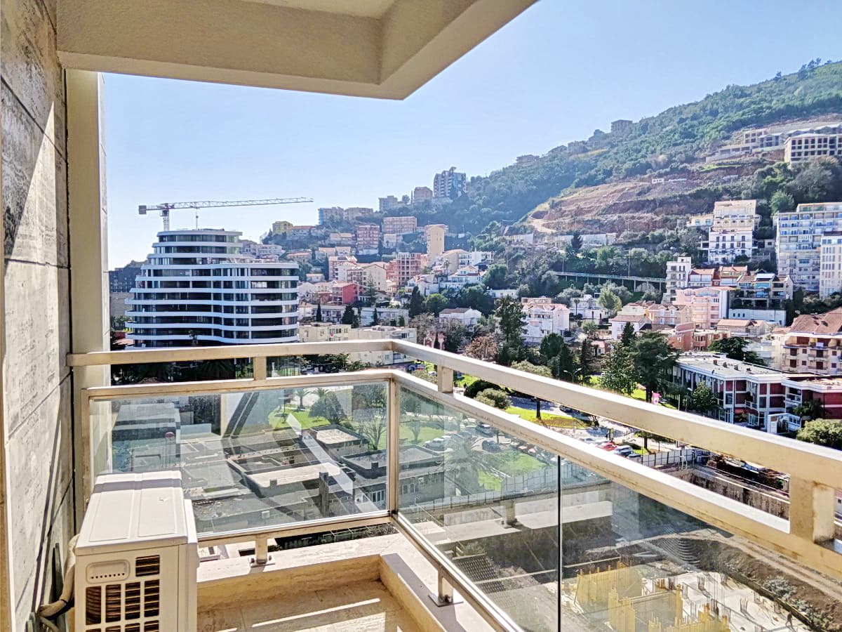 Вид с балкона квартиры в Будве, Черногория: панорама города, горный пейзаж и современная архитектура жилого комплекса.
