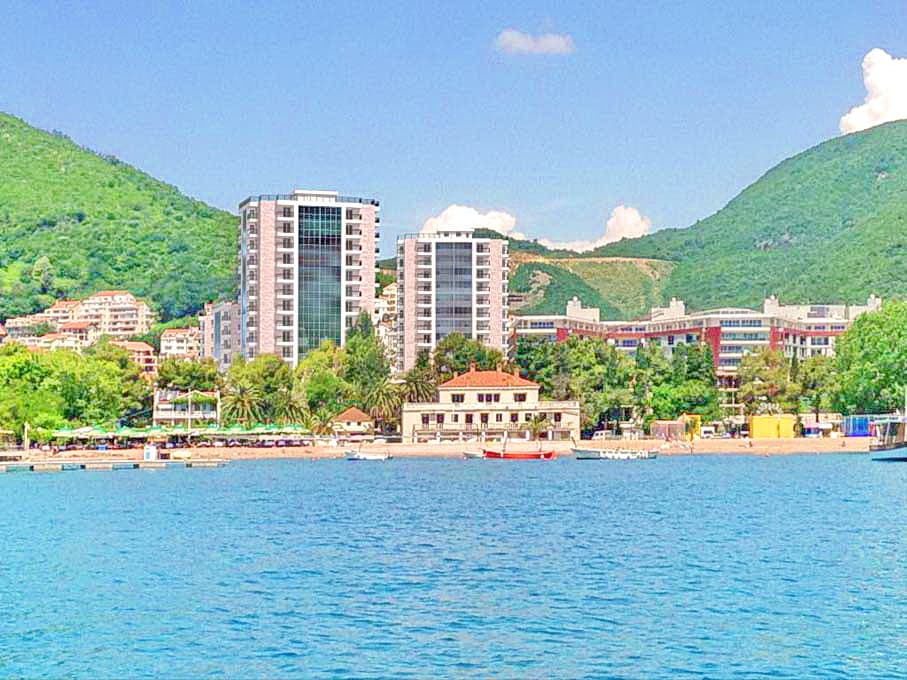 Вид с моря на современные жилые комплексы и пляж в Будве, Черногория: панорама побережья с горами и инфраструктурой.