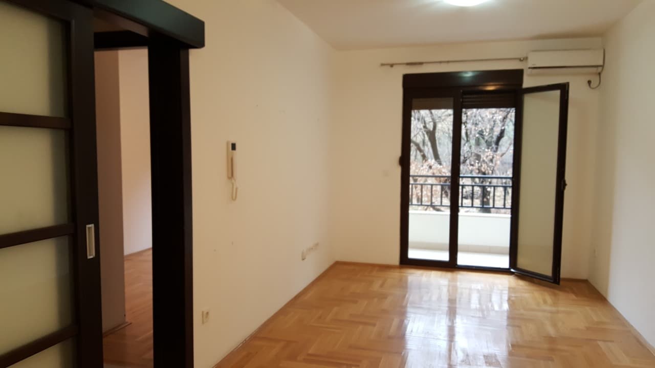 Светлая пустая комната с паркетом, выходом на балкон и кондиционером в квартире в Будве, Черногория.