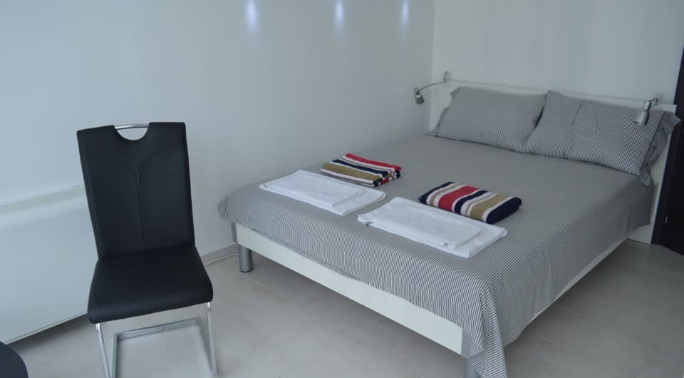 Спальня с двуспальной кроватью и черным стулом на вилле в Тивате, Черногория. Современный интерьер в светлых тонах.