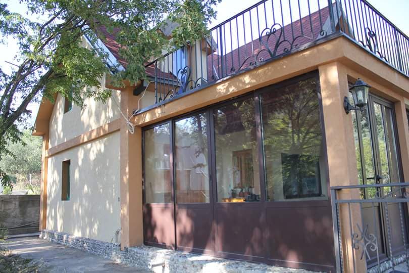 Двухэтажный дом в Сутоморе, Черногория, с панорамным остеклением, террасой и коваными перилами на втором этаже.