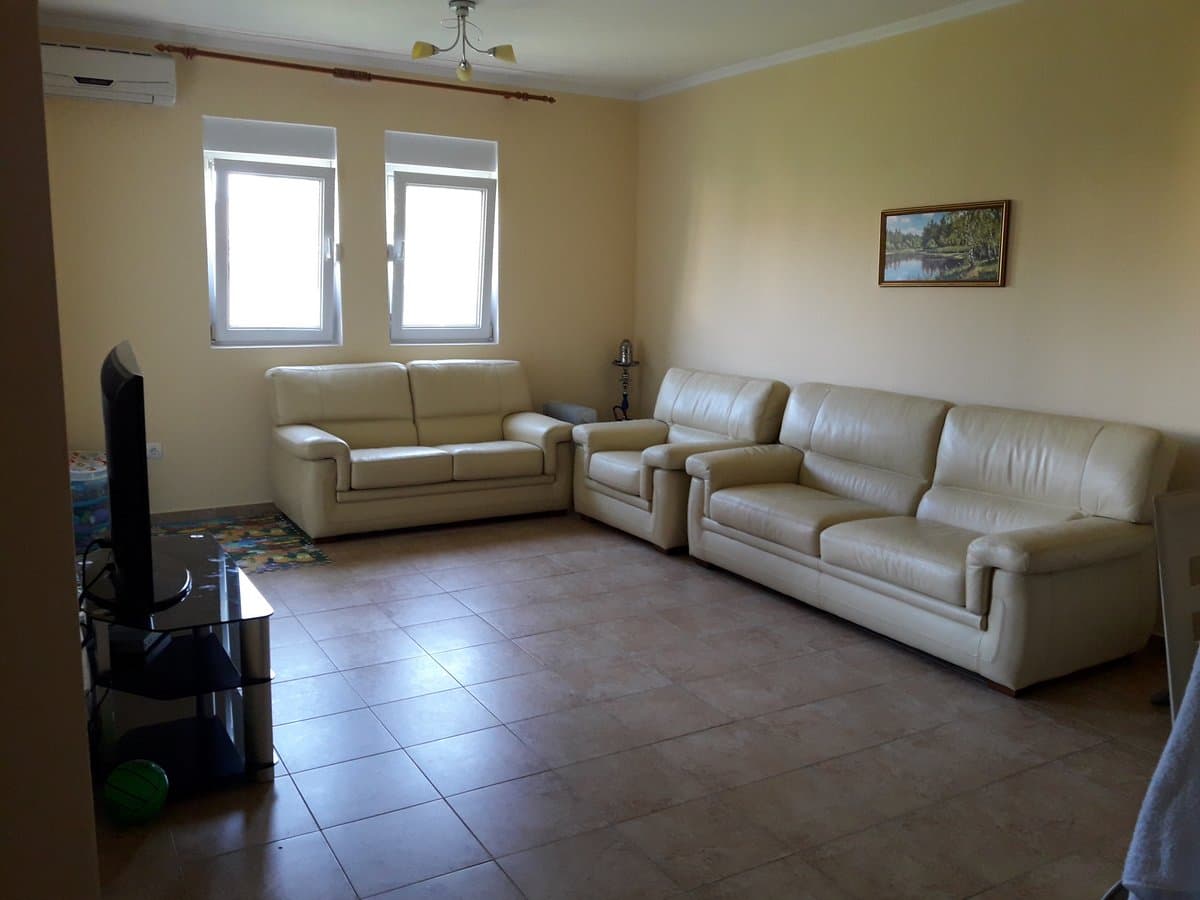 Светлая гостиная с кожаными диванами в квартире на продажу, Баошичи, Черногория. Плиточный пол, ТВ-зона и окна.