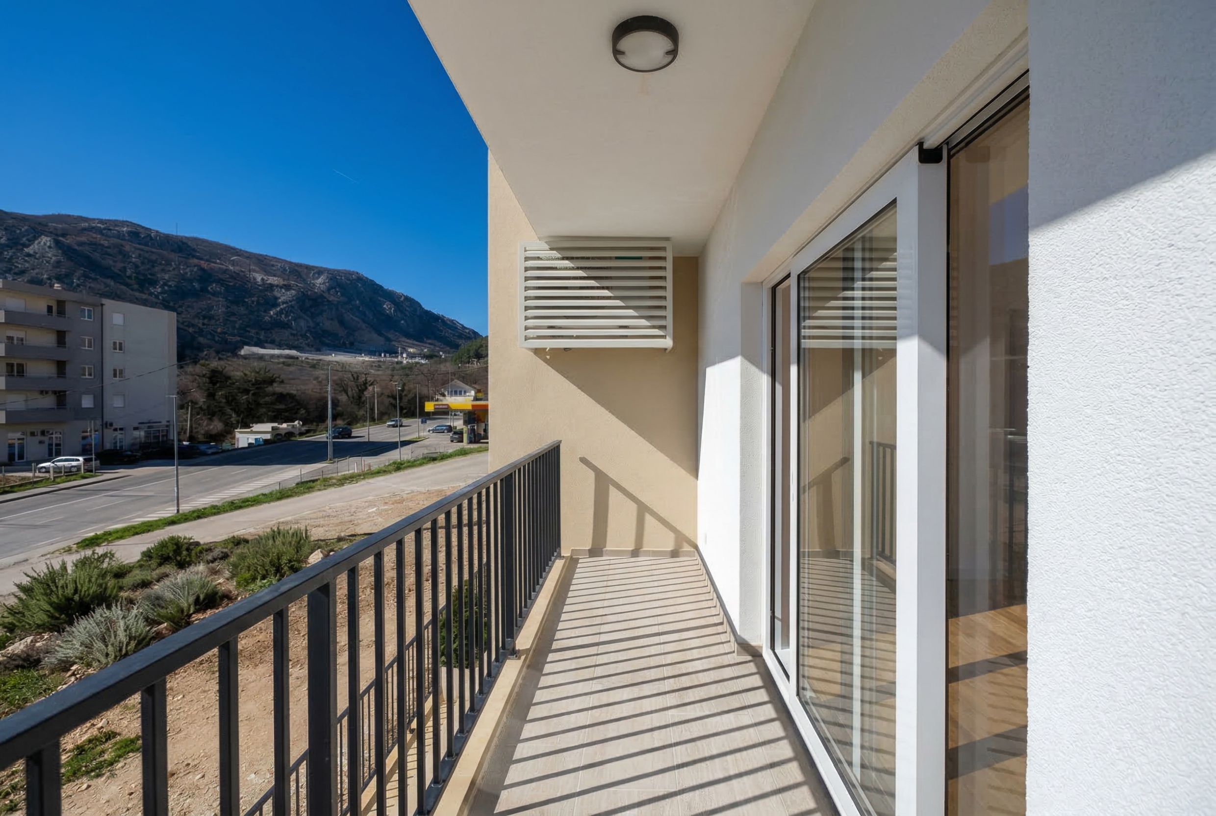 Apartment balcony in Sutomore, Montenegro: panoramic windows, tiled floor, metal railings, and mountain view.