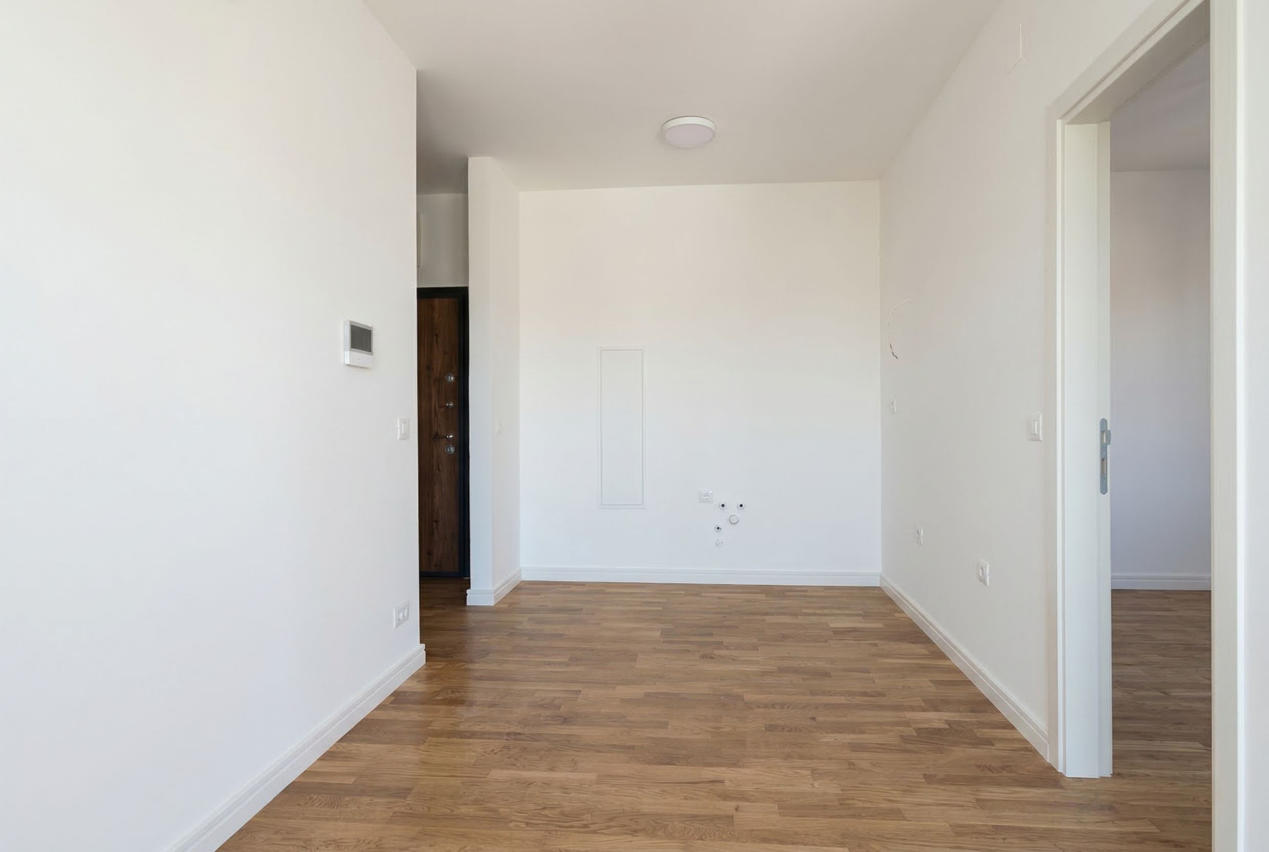 Bright living room with wood-effect finishes in a new apartment in Sutomore, Montenegro: view of an empty room with parquet flooring.