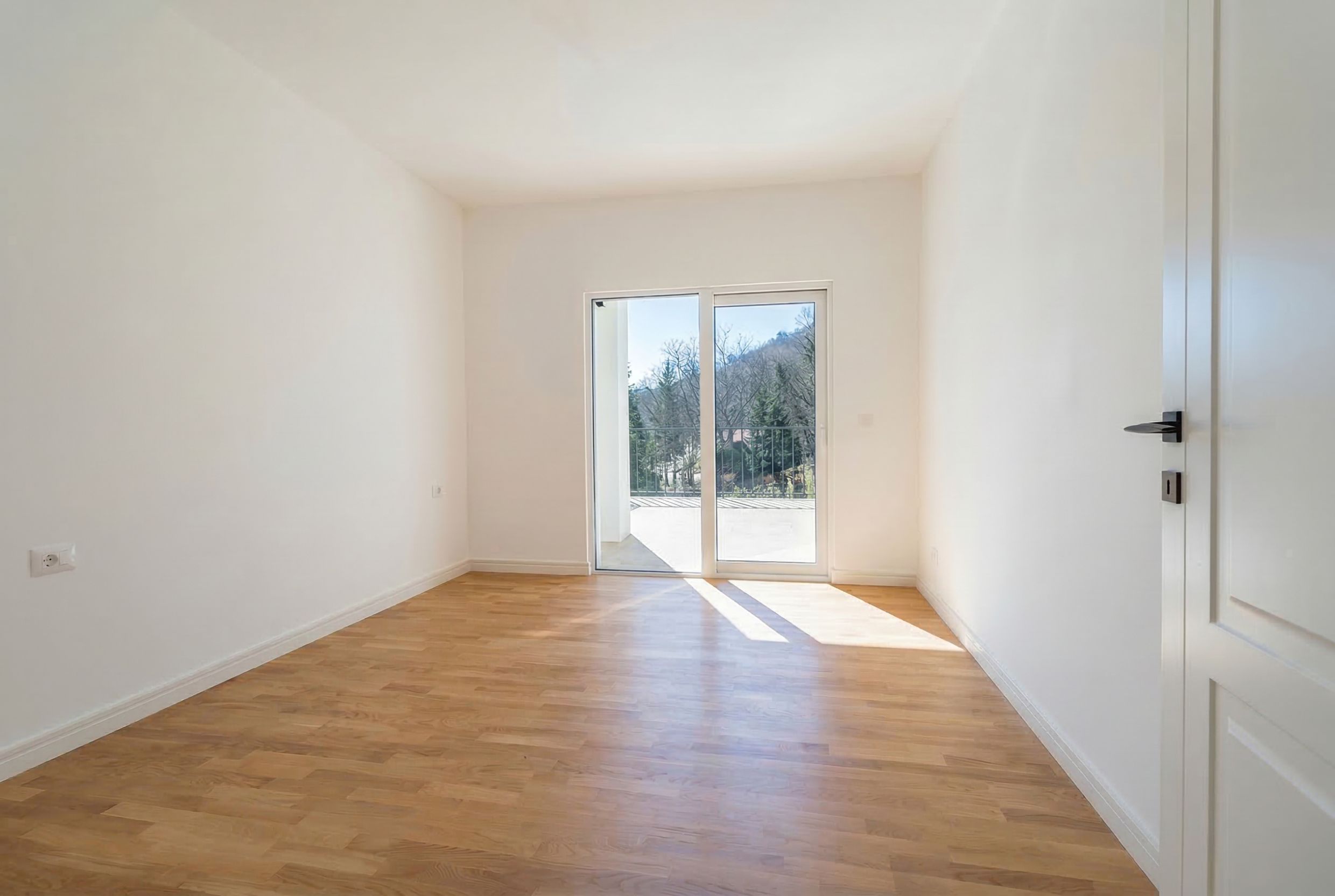 Bright empty bedroom with parquet flooring and access to a terrace in an apartment in Sutomore, Montenegro.