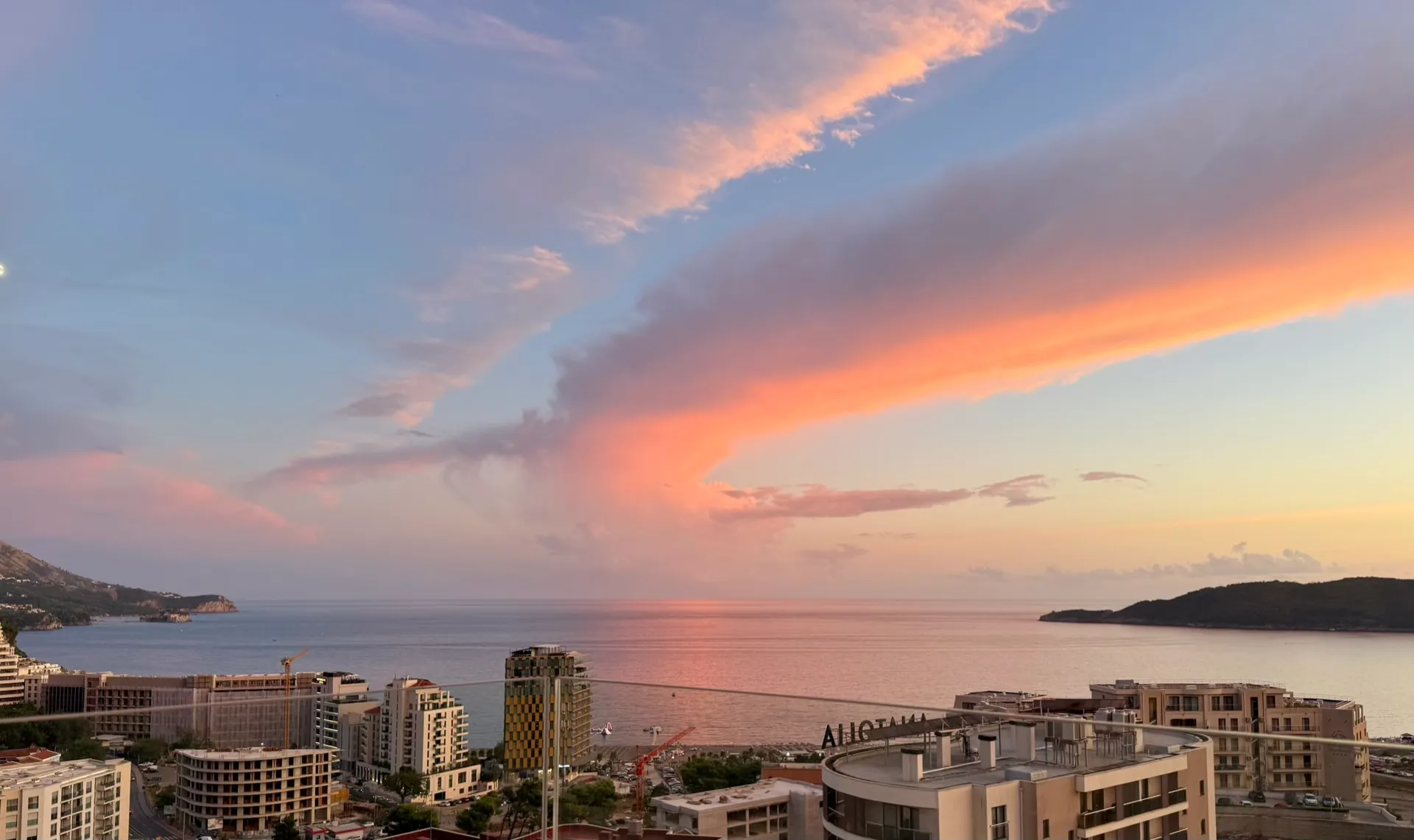 Panoramic view of the sea and city buildings against a sunset sky with orange clouds.
